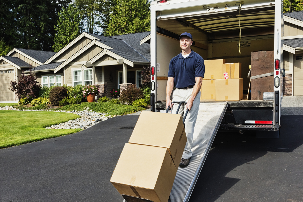 A mover unloading the truck, walking cardboard boxes down the ramp on a hand truck.